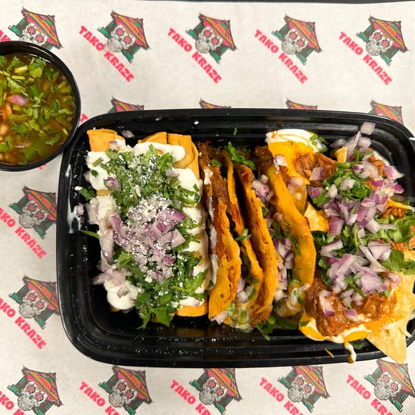 A black tray of Tako Kraze Mexican food with tacos, nachos, and a side of consommé.