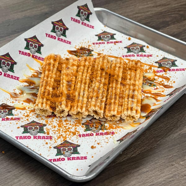 Tako Kraze churros, drizzled with sauce and cinnamon sugar, on branded parchment paper.