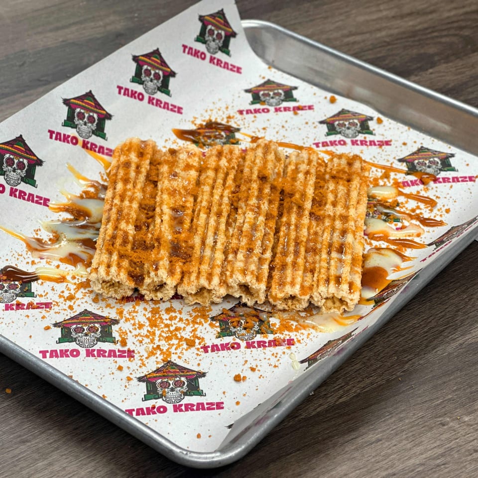 Tako Kraze churros, drizzled with sauce and cinnamon sugar, on branded parchment paper.