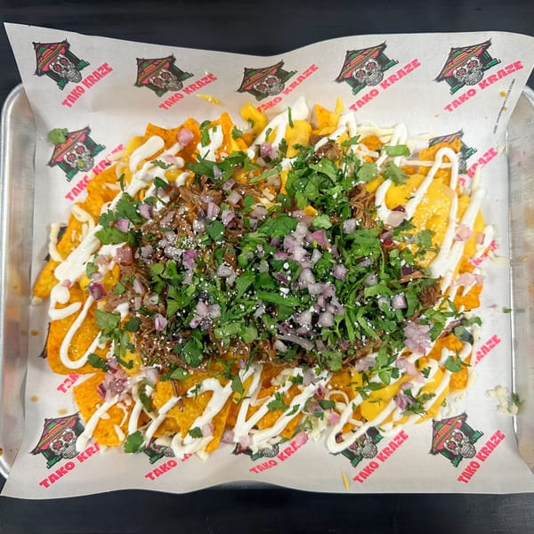 Tako Kraze nachos with shredded meat, cilantro, red onions, and white sauce on branded paper.